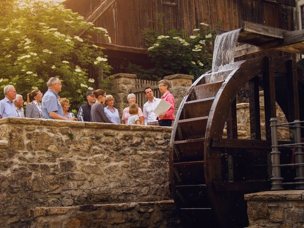 Gruppe lauscht einer historischen Stadtführung am idyllischen Mühlenrad in Bad Driburg.