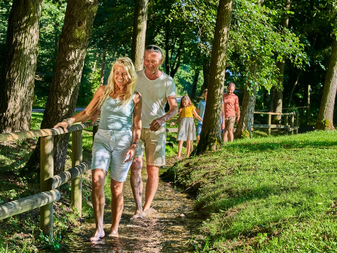 Barfußpfad Bad Wünnenberg für Groß und Klein Personen genießen einen naturbelassenen Barfußpfad, umgeben von Bäumen und sommerlichem Grün.