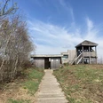 Oppenweher Moor Holzweg führt zu einem Aussichtspunkt mit Pavillon im Oppenweher Moor, umgeben von Bäumen und blauem Himmel.