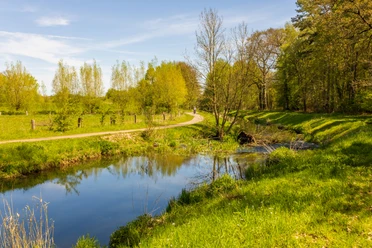 Naherholungsgebiet Große Aue Ein ruhiger Fluss schlängelt sich durch eine grüne, baumbestandene Landschaft. Ein Wanderweg führt entlang.