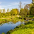 Naherholungsgebiet Große Aue Ein ruhiger Fluss schlängelt sich durch eine grüne, baumbestandene Landschaft. Ein Wanderweg führt entlang.