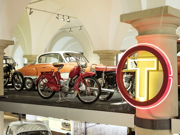 Vintage cars and motorcycles in a bright showroom with a classic design.