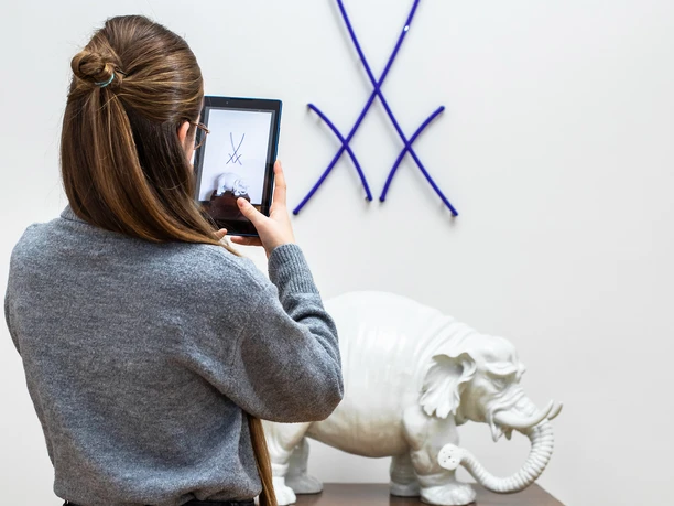 Tablet Rallye Eine Frau fotografiert eine Ausstellung mit einem Tablet, im Fokus ein weißer Porzellan-Elefant.