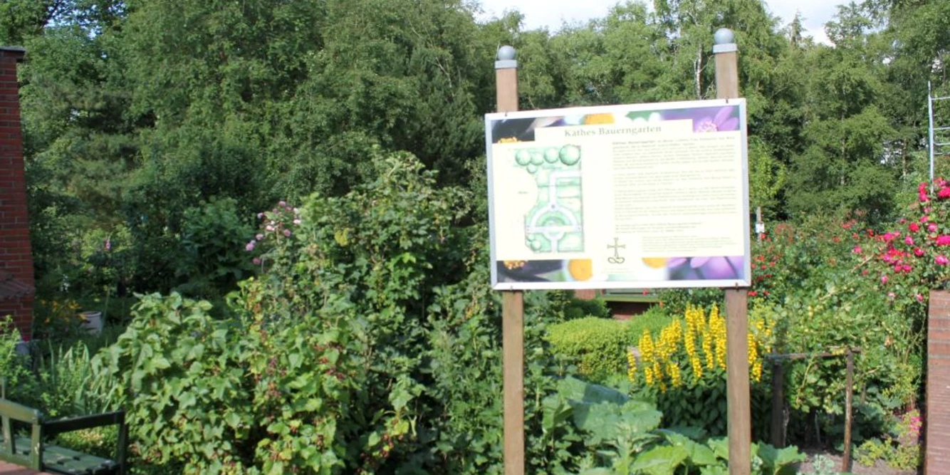 Garten des Nazareners in Twist - Blick auf Käthes Bauerngarten ©Emsland Tourismus GmbH.jpg Informative Tafel inmitten eines blühenden Bauerngartens mit Sträuchern, Stauden und Bäumen.