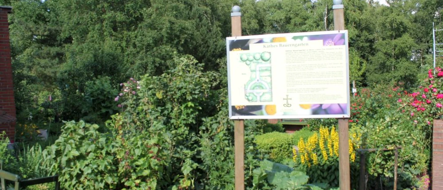 Garten des Nazareners in Twist - Blick auf Käthes Bauerngarten ©Emsland Tourismus GmbH.jpg Informative Tafel inmitten eines blühenden Bauerngartens mit Sträuchern, Stauden und Bäumen.