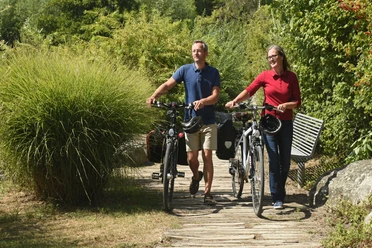 EmsRadweg-56-Themenmanagement-Radfahren-Teutoburger-Wald-F-Grawe.jpg Paar schiebt Fahrräder auf einem naturbelassenen Pfad, umgeben von grüner Vegetation.