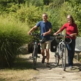 EmsRadweg-56-Themenmanagement-Radfahren-Teutoburger-Wald-F-Grawe.jpg Paar schiebt Fahrräder auf einem naturbelassenen Pfad, umgeben von grüner Vegetation.