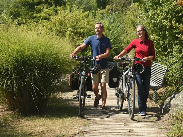 EmsRadweg-56-Themenmanagement-Radfahren-Teutoburger-Wald-F-Grawe.jpg Paar schiebt Fahrräder auf einem naturbelassenen Pfad, umgeben von grüner Vegetation.