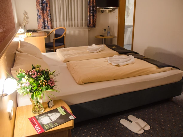 Landhaus Begatal Zimmer CC BY-SA - Büker.jpg Hotelzimmer im Landhaus Begatal mit Doppelbett, Blumen, Schreibtisch und TV