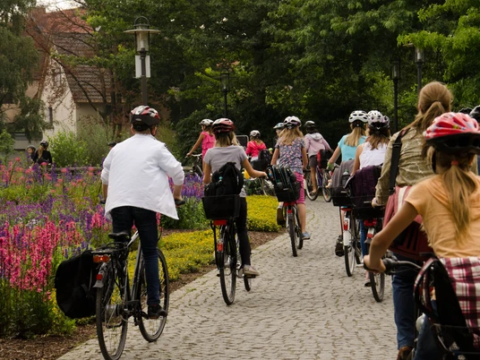 Radgruppe im Flora-Westfalica-Park Eine Gruppe von Radfahrern, darunter Kinder und Erwachsene, fährt auf einem blumenumrandeten Weg.