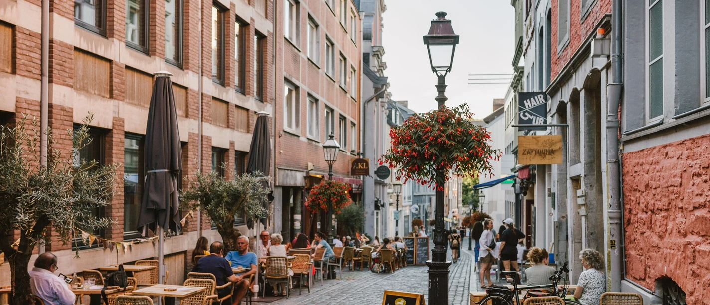 Pontstraße.jpg Lebendige Fußgängerzone mit Kopfsteinpflaster, umrahmt von Cafés, Menschen und üppigen Blumenarrangements.