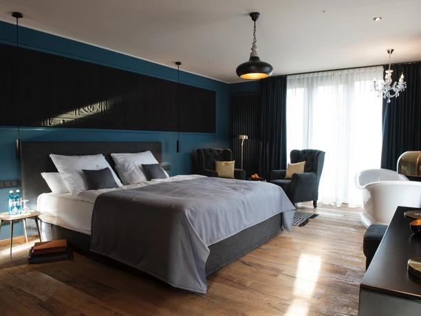 Hamm2022_GutSternholz02_CCBYSA_GutSternholzGmbH.jpg Doppelzimmer mit grauem Bett, Holzboden und natürlichem Licht durch große Fenster.
