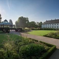 Schloss Benkhausen Schloss Benkhausen mit gepflegtem Garten und Pavillon bei Sonnenschein, umgeben von Bäumen und Blumen.