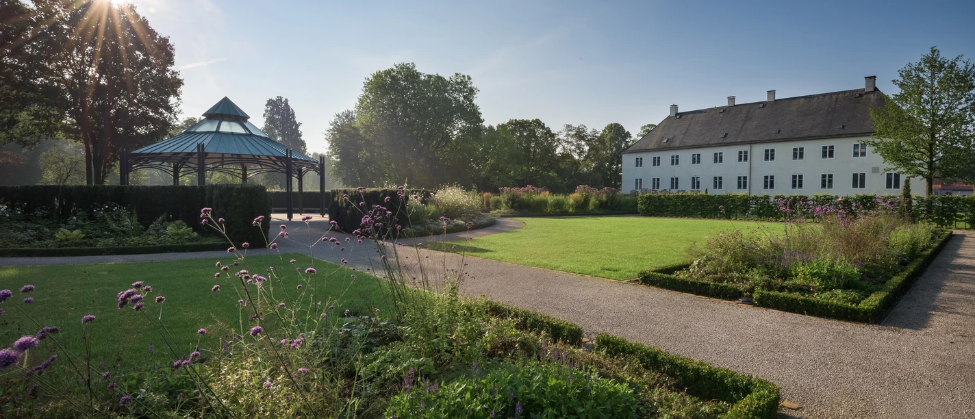 Schloss Benkhausen Schloss Benkhausen mit gepflegtem Garten und Pavillon bei Sonnenschein, umgeben von Bäumen und Blumen.