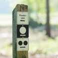 Stemweder Berg Holzpfosten mit Wandertafel und zwei Orientierungsschildern im Grünen, weicher Hintergrund.