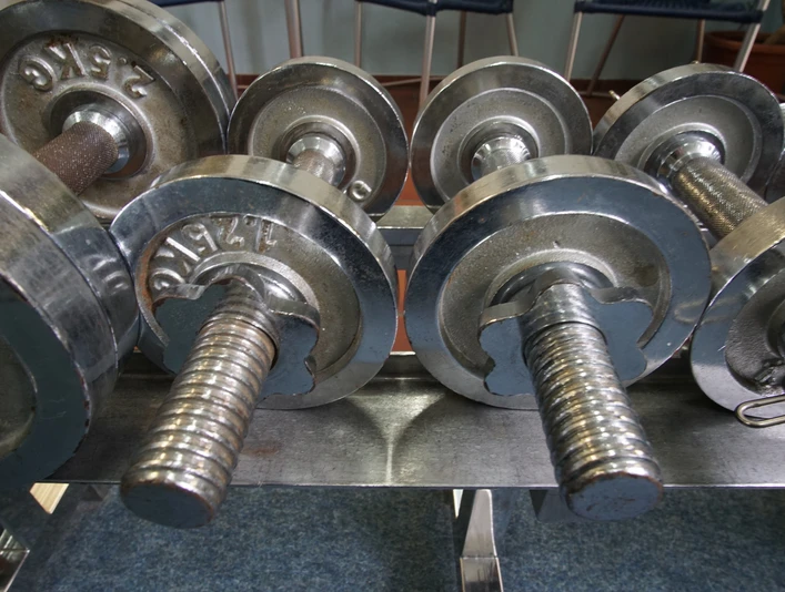 BodyTop Das Bild zeigt mehrere silberne Hanteln, die in einem Fitnessstudio aufgereiht sind.