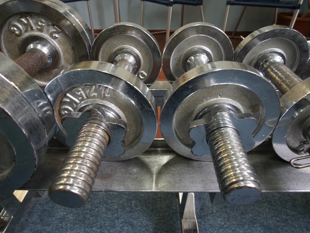 Das Bild zeigt mehrere silberne Hanteln, die in einem Fitnessstudio aufgereiht sind.