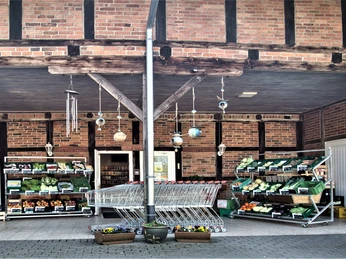 Bauckhof Auf dem Bild ist der Eingang eines Hofladens zu sehen. Es zeigt Einkaufswagen und Regale voller frischem Gemüse.