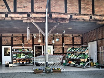 Bauckhof Auf dem Bild ist der Eingang eines Hofladens zu sehen. Es zeigt Einkaufswagen und Regale voller frischem Gemüse.