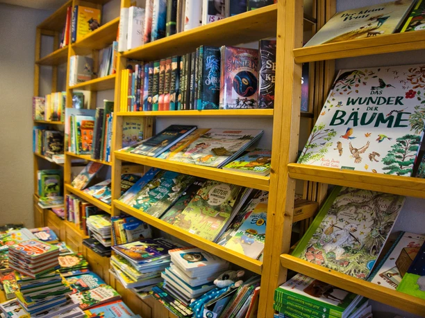 Planken vol kinderboeken in een boekhandel. De boeken liggen en staan opgestapeld.