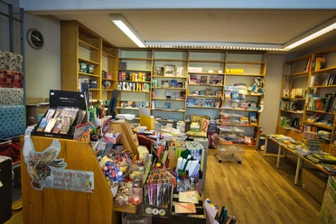 Einblick in die Bücherstube Eine gemütliche Bücherstube mit voll bepackten Regalen, die bunte Bücher und Schreibwaren präsentieren.