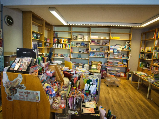 Einblick in die Bücherstube Eine gemütliche Bücherstube mit voll bepackten Regalen, die bunte Bücher und Schreibwaren präsentieren.