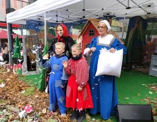 Kinder und Erwachsene in Märchenkostümen stehen unter einem Pavillon, umgeben von Herbstlaub.