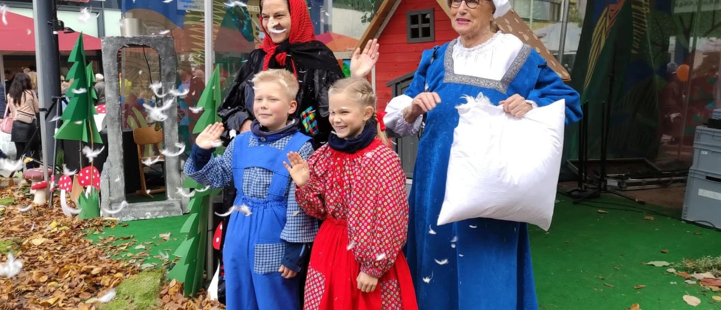 Kinder und Erwachsene in Märchenkostümen stehen unter einem Pavillon, umgeben von Herbstlaub.