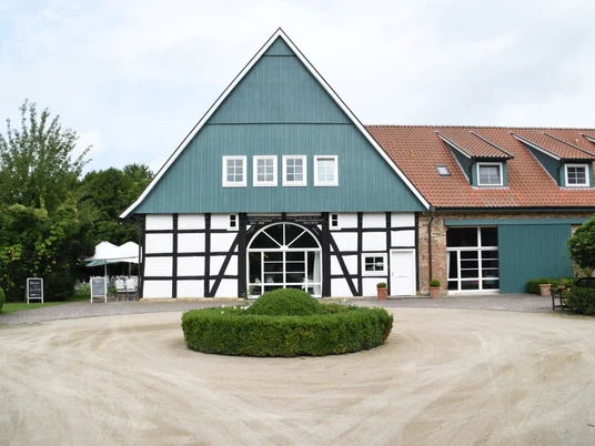 Historisches Fachwerkgebäude mit grünem Giebel, gepflegtem Garten und Kiesauffahrt im Vordergrund.