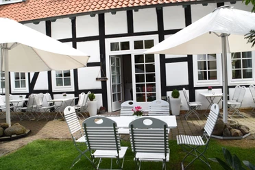 Bühlmeyer_2.JPG Gepflegte Terrasse mit weiß-schwarzem Fachwerkhaus, Tischen, Stühlen und Sonnenschirmen im Garten.