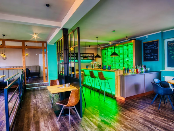 Jamies Burger Moderner Gastraum mit grün beleuchteter Bar, dunklem Holzboden und Sitzgruppen.