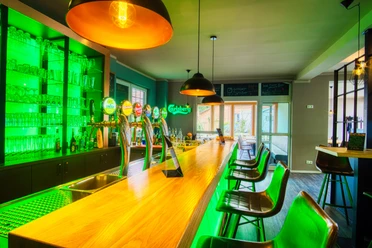 Innenansicht Moderne Bar mit langer Holzteke, grüner LED-Beleuchtung und schwarzen Barhockern.