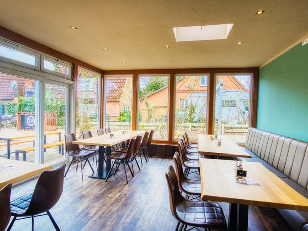 Jamies Burger Heller Gastraum mit bodentiefen Fenstern, Holztischen und braunen Lederstühlen in Amelinghausen.