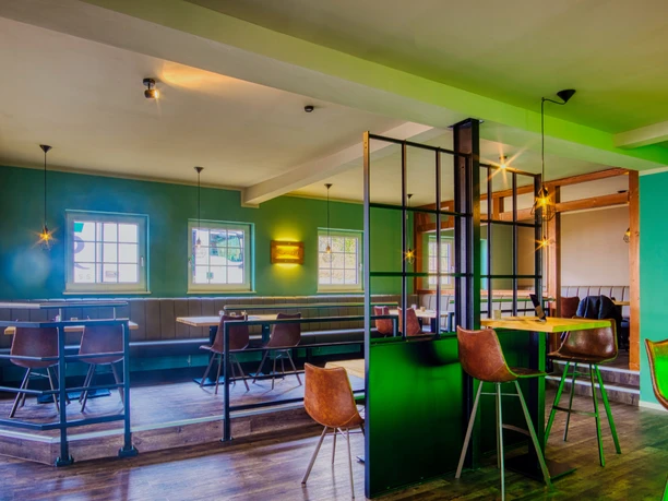 Jamies Burger Moderner Gastraum mit grünen Wänden, dunklen Holzelementen, Lederstühlen und schwarzen Metallakzenten.