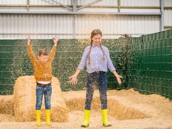 Spaß & Abenteuer auf Gut Hixholz in Velbert Zwei Kinder mit leuchtend gelben Gummistiefeln spielen fröhlich in einem Raum voller Stroh.