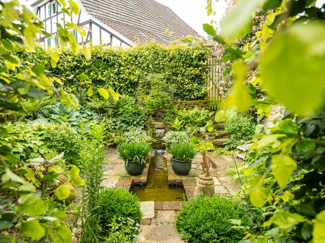 Ferienwohung Hof Tüschenbonnen Ein gepflegter, grüner Garten mit Teich und üppiger Bepflanzung in einem rustikalen Ambiente.
