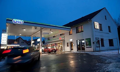 OIL-INN.jpg Eine Tankstelle im Abendlicht mit mehreren Zapfsäulen, daneben ein Gebäude aus weißem Putz.