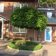 Apartment Bärenhöhle.JPG Rotes Backsteinhaus mit blauen und weißen Türen, gepflegtem Vorgarten und Baum in der Mitte.