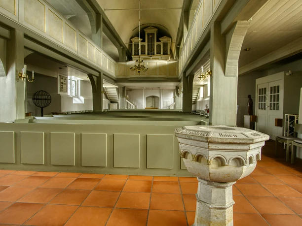 Taufbecken Das Bild zeigt ein kunstvoll verziertes steinernes Taufbecken in einer historischen Kirche mit Holzbänken.