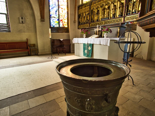 Innenansicht Altes, bronzenes Taufbecken im Kirchenschiff vor dem reich verzierten Schnitzaltar.