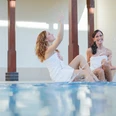 Bad-Oeynhausen-Bali-Therme-Bewegungsbecken-1-Bali-Therme-GmbH.jpg Zwei Frauen sitzen lachend am Rande eines Poolbeckens in der Bali Therme Bad Oeynhausen.