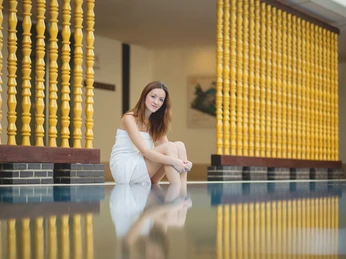 Bad-Oeynhausen-Bali-Therme-Entspannungsbecken-Bali-Therme-GmbH.jpg Eine Frau im weißen Handtuch sitzt entspannt am Rande eines Schwimmbeckens mit gelben Säulen.