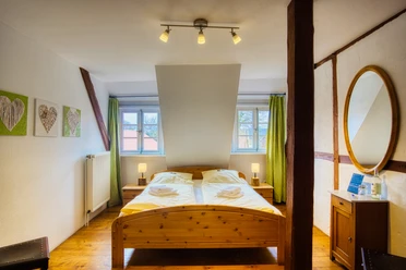 Doppelzimmer Doppelzimmer mit Holzbett, sichtbaren Holzbalken, Holzboden und grünen Vorhängen.