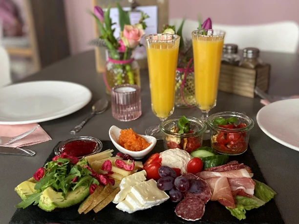 Eine reichhaltige Frühstücksplatte mit Käse, Wurst, Avocado und Obst sowie zwei Gläser Orangensaft.