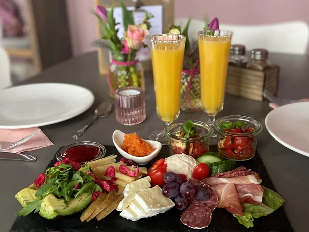Frühtsücks-Variation Eine reichhaltige Frühstücksplatte mit Käse, Wurst, Avocado und Obst sowie zwei Gläser Orangensaft.