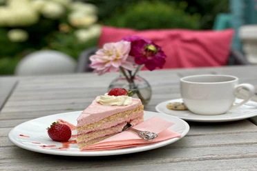 Kuchen Ein Stück Erdbeersahnetorte mit frischen Erdbeeren und einer Tasse Kaffee auf einem Gartentisch.