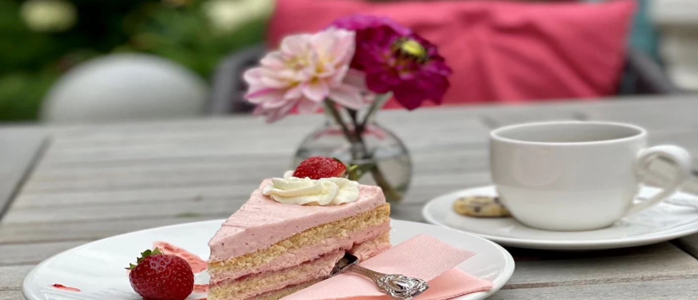 Kuchen Ein Stück Erdbeersahnetorte mit frischen Erdbeeren und einer Tasse Kaffee auf einem Gartentisch.