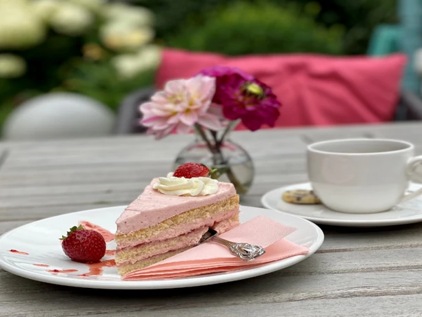Kuchen Ein Stück Erdbeersahnetorte mit frischen Erdbeeren und einer Tasse Kaffee auf einem Gartentisch.