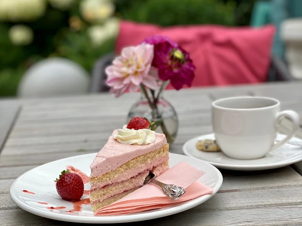 Kuchen Ein Stück Erdbeersahnetorte mit frischen Erdbeeren und einer Tasse Kaffee auf einem Gartentisch.