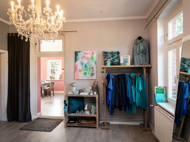 Laden-Kamelotta Kleiner Ladenbereich im Café mit blauer Kleidung an einer Garderobe und hellem Kronleuchter.